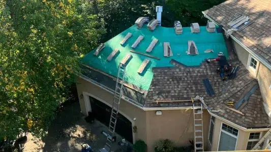 Drone view of shingle roof replacement in progress with ladders and roofers working, by XL Home Improvements.