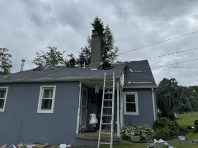 Front view of a residential home in Skippack, PA, with roofers installing new Biscayne Blue GAF Timberline HDZ shingles after ice and water shield, synthetic underlayment, and fresh edging installation.