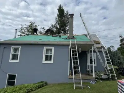 Front view of a residential home in Skippack, PA, with roofers tearing off old shingles in preparation for a full shingle roof replacement.