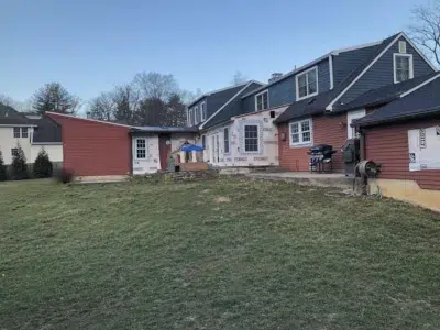 Backside view of a Berwyn, PA home showing new windows installed by Wolf Home Pros and old siding being removed from the first story by XL Home Improvements.