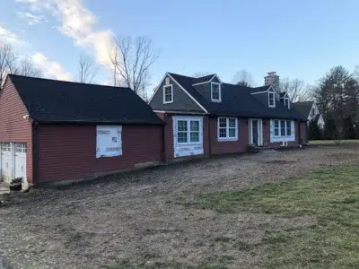 Distant view of a residential home in Berwyn, PA with old siding removed around the garage and windows as part of a siding replacement project by XL Home Improvements.