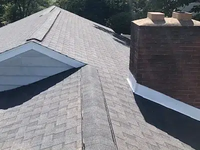 Closeup view of clean shingle installation around the chimney and new ridge vents along the peaks of a brand-new shingle roof replacement in Perkasie, PA.