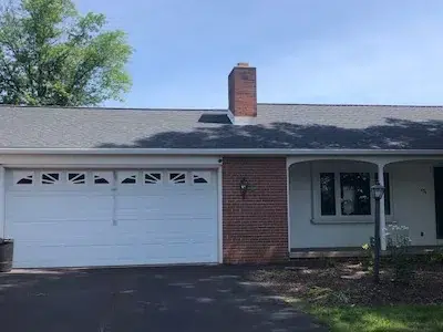 Front view of a home with a new shingle roof installation, featuring the chimney and visible from the driveway.