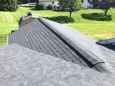 Closeup of a new ridge vent on the side of a shingle roof, overlooking the yard with a shed in the distance.