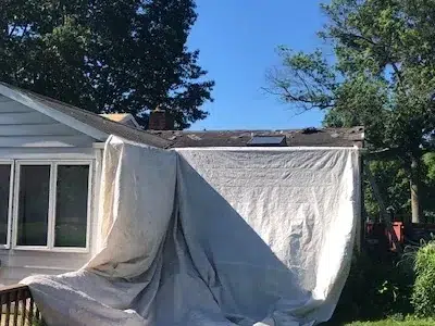 Backside view of a residential home showing the original roof with a tarp set up in preparation for a shingle roof replacement.