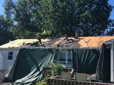 Roofers removing old shingles with tarps draped from the roof to protect the homeowner’s property during a shingle roof replacement.